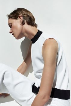 Woman with short hair wearing a white top with a black collar and white pants
