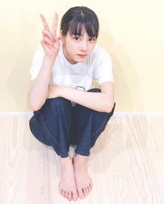 Woman with black hair and bangs making a peace sign while sitting on the floor