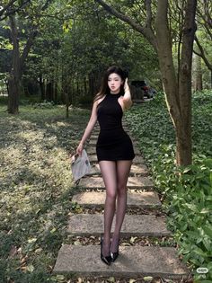 Woman in a black mini dress and high heels walking on a forest path