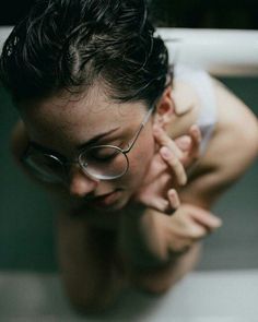 Person with wet black hair and glasses looking down in soft indoor lighting