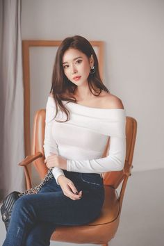 Woman with long hair wearing an off-shoulder top and jeans, sitting indoors