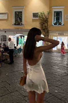 Woman in a white mini dress with an open back on a street at night