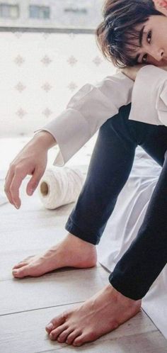 Person in a white shirt and black pants sitting on the floor with bare feet
