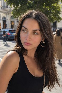 Woman with long brown hair and hoop earrings in a black tank top outdoors