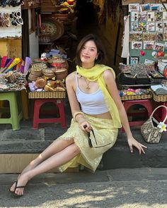 Woman in a yellow skirt and white tank top sitting in front of a market stall