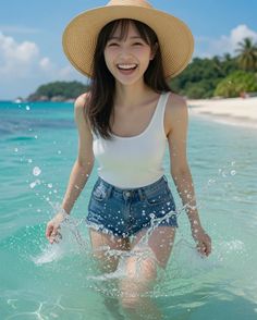 Woman in a straw hat and denim shorts splashing in clear beach water