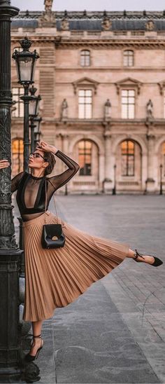 Woman in a sheer top and pleated skirt posing outdoors