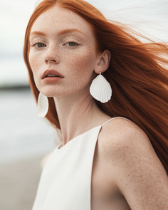 Woman with red hair and freckles wearing a white dress and shell earrings outdoors