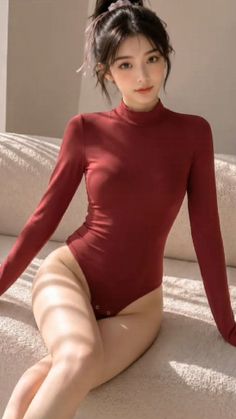 Woman in a red long-sleeved bodysuit sitting on a couch with soft lighting