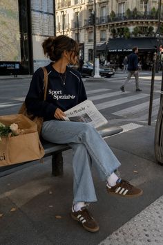 Woman in a sweatshirt and jeans sitting on a bench on a city street
