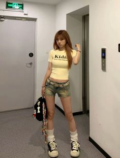 Woman in a yellow crop top and denim shorts standing indoors