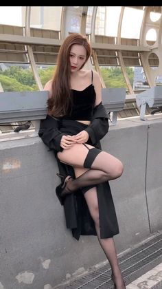 Woman in a black top and coat with stockings and high heels posing outdoors