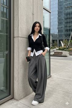 Woman in a black top and wide leg pants holding a coffee cup outdoors