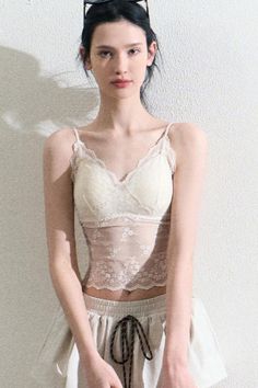 Woman in a lace top and shorts against a white wall