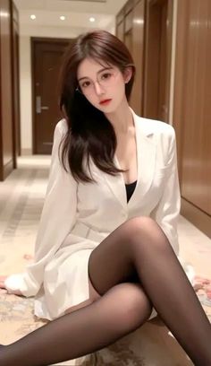 Woman in a white blazer and black stockings sitting on the floor indoors