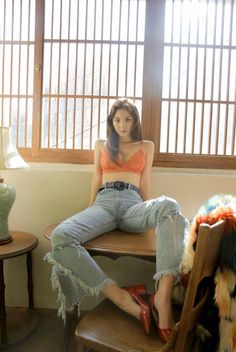 Woman in a lace bralette and ripped jeans sitting on a table indoors