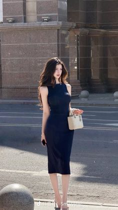 Woman in a black dress holding a white handbag on a city street