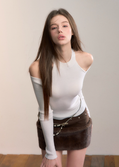 Woman with long hair wearing a white top and brown skirt with a pearl chain