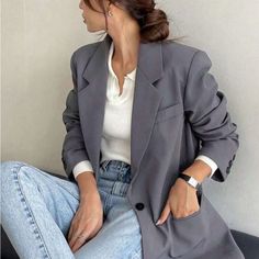Woman in a gray blazer, white top, and light wash jeans with hair in a bun