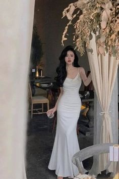 Woman in a white dress with long dark hair standing indoors