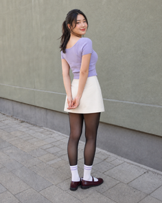 Woman in a purple top and white mini skirt with black tights and mary jane shoes