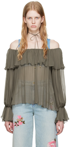 Woman with blonde hair wearing an off-shoulder sheer top and embroidered jeans