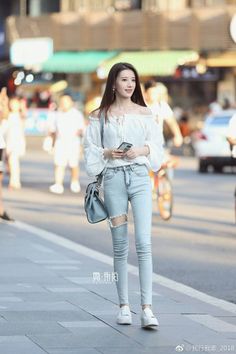 Woman with long hair wearing an off-shoulder top and ripped jeans on a street