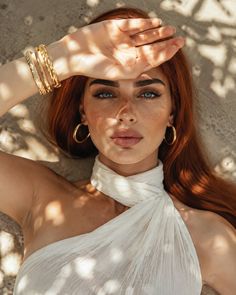 Woman with red hair and blue eyes in a white dress, shielding her face from the sun