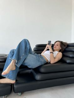 Woman with short hair in a white tank top and blue jeans lying on a black sofa