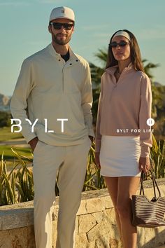 A couple posing outdoors on a sunny day, wearing casual athletic attire
