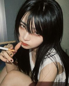 Woman with long black hair and bangs holding a cigarette