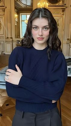 Woman with long dark hair wearing a navy blue top and jewelry in an elegant indoor setting
