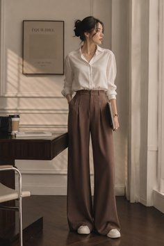 Woman in a white shirt and brown wide-leg pants standing indoors