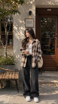 Woman in a plaid shirt and wide leg jeans holding a coffee cup outside a cafe