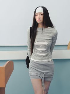 Woman with long black hair and a white headband wearing a striped cut-out top and grey skirt