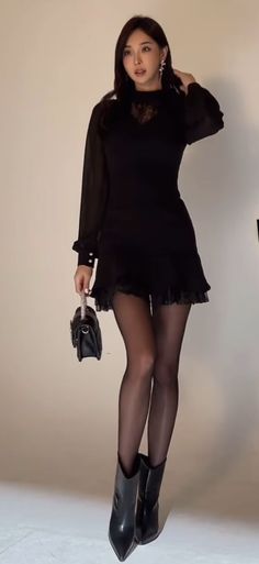Woman in a black dress and tights holding a small handbag
