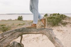 Person in jeans and barefoot shoes walking on driftwood on a sandy beach