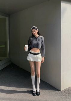 Woman in a white pleated skirt and crop top holding a coffee cup outdoors