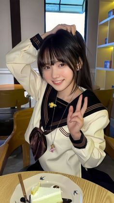Girl in a school uniform with a ponytail, smiling and holding up a peace sign