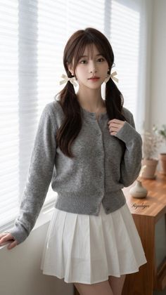 Woman with twin tails wearing a grey cardigan and white pleated skirt indoors