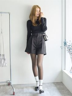 Woman in a black top and shorts with tights and white socks posing indoors