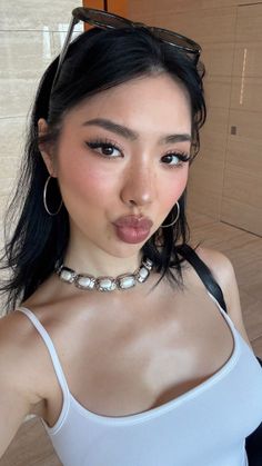 Woman with black hair and a white tank top making a pouty face