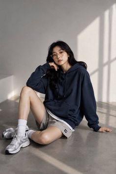 Woman with long dark hair wearing a hoodie and shorts, sitting on the floor