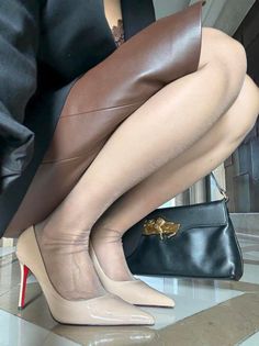 Woman in a brown leather skirt and nude pantyhose with high heels and a black handbag