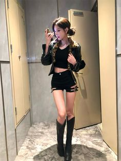 Woman in a leather jacket, crop top, and short shorts in an indoor setting