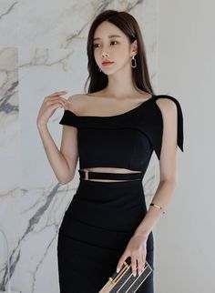 Woman in a black off-shoulder dress with a cut-out waist holding a clutch bag