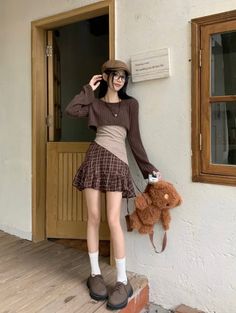 Woman in a plaid skirt and crop top holding a teddy bear bag outdoors