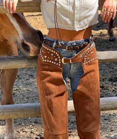 Person in cowboy chaps and a cropped top next to a horse