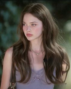 Young woman with long brown hair wearing a camisole and pearl necklace outdoors