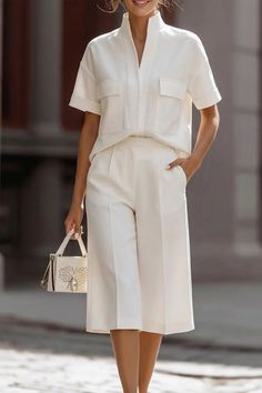 Woman in a white short-sleeve shirt and culottes holding a small handbag